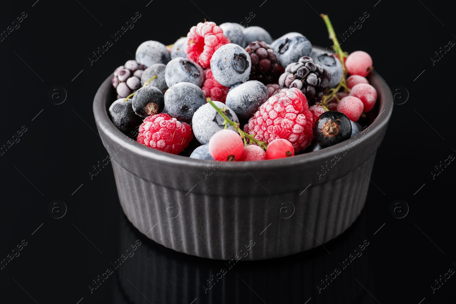 Photo of Many different frozen berries in bowl on black table, closeup