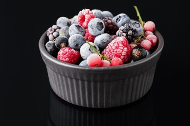 Photo of Many different frozen berries in bowl on black table, closeup