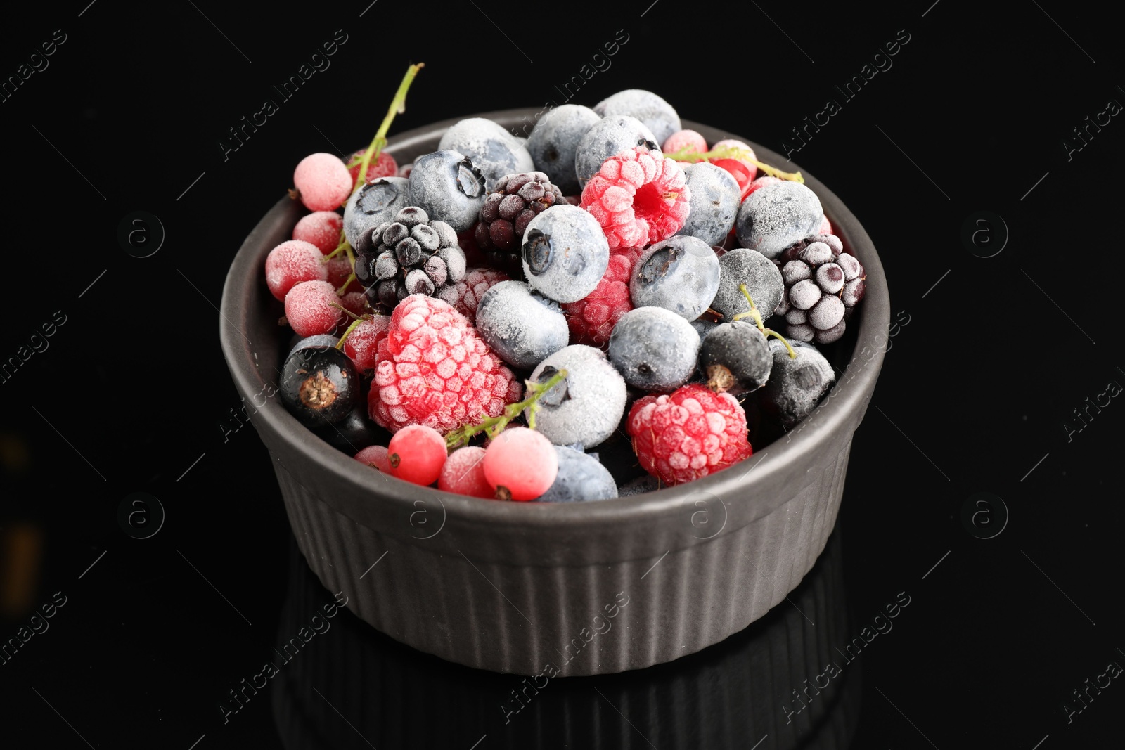 Photo of Many different frozen berries in bowl on black table, closeup