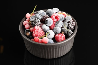 Photo of Many different frozen berries in bowl on black table, closeup
