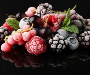 Photo of Many different frozen berries and mint on black table, closeup