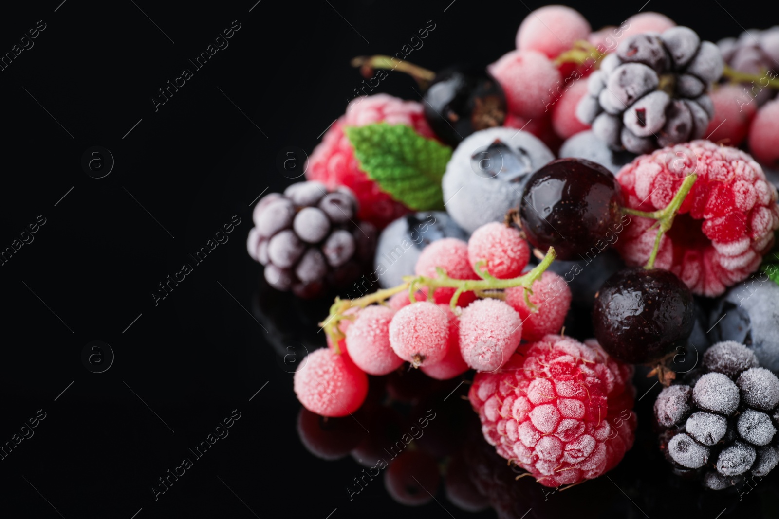 Photo of Many different frozen berries on black table, closeup. Space for text