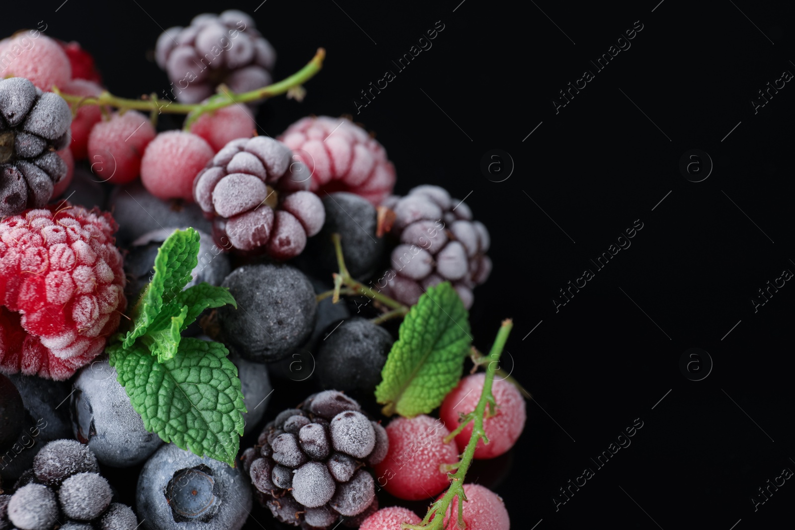 Photo of Many different frozen berries and mint on black table, closeup. Space for text