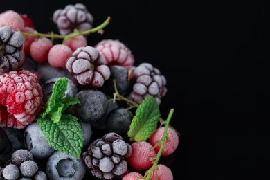 Photo of Many different frozen berries and mint on black table, closeup. Space for text