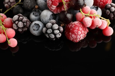 Photo of Many different frozen berries on black table, closeup. Space for text