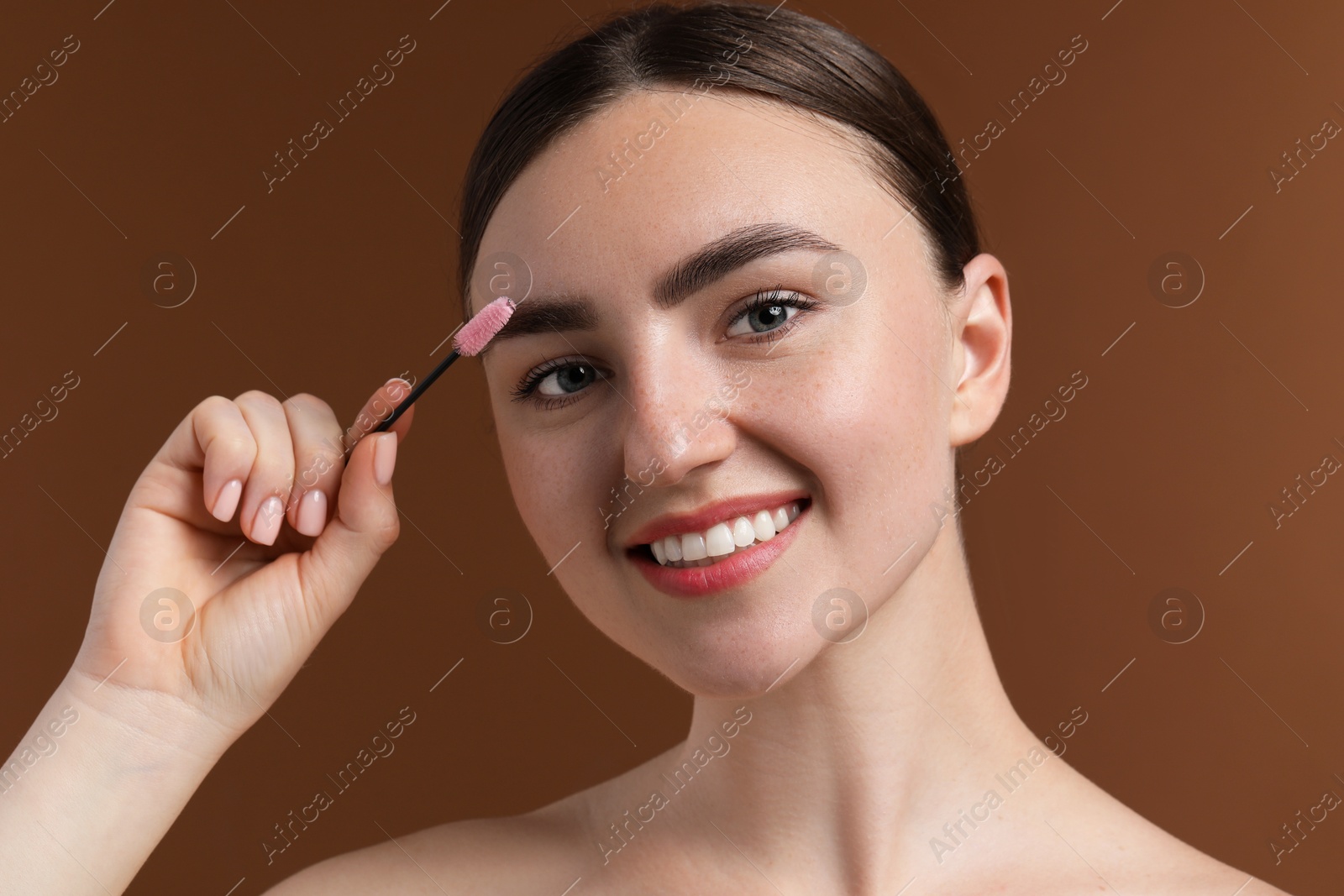 Photo of Young woman brushing her eyebrow with spoolie on brown background