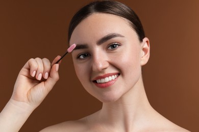 Photo of Young woman brushing her eyebrow with spoolie on brown background