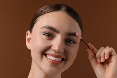 Photo of Young woman brushing her eyebrow with spoolie on brown background