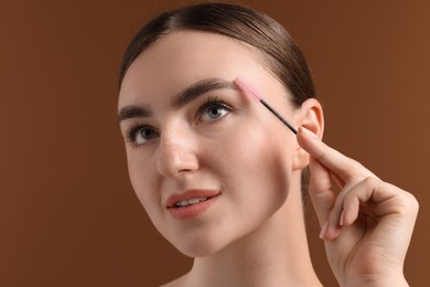 Photo of Young woman brushing her eyebrow with spoolie on brown background, closeup