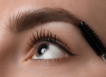 Photo of Young woman brushing her eyebrow with spoolie, closeup