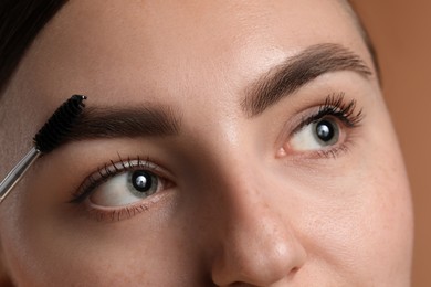 Photo of Young woman brushing her eyebrow with spoolie on brown background, closeup