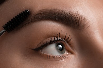 Photo of Young woman brushing her eyebrow with spoolie, closeup