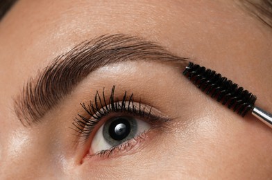 Photo of Young woman brushing her eyebrow with spoolie, closeup