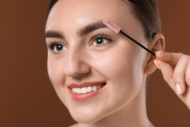 Photo of Young woman brushing her eyebrow with spoolie on brown background, closeup