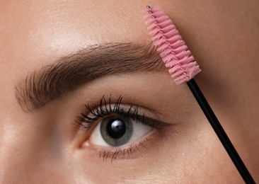 Photo of Young woman brushing her eyebrow with spoolie, closeup