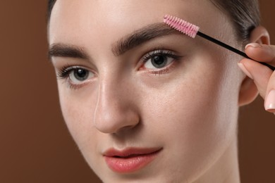 Photo of Young woman brushing her eyebrow with spoolie on brown background, closeup