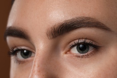 Photo of Young woman with beautiful eyebrows on brown background, closeup
