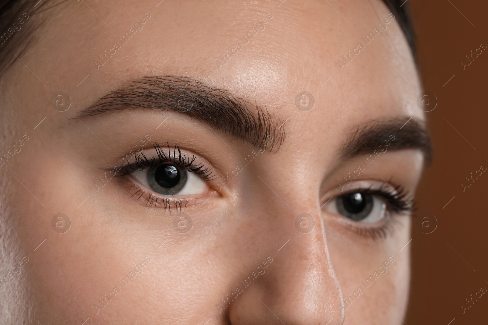 Photo of Young woman with beautiful eyebrows on brown background, closeup