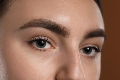 Photo of Young woman with beautiful eyebrows on brown background, closeup