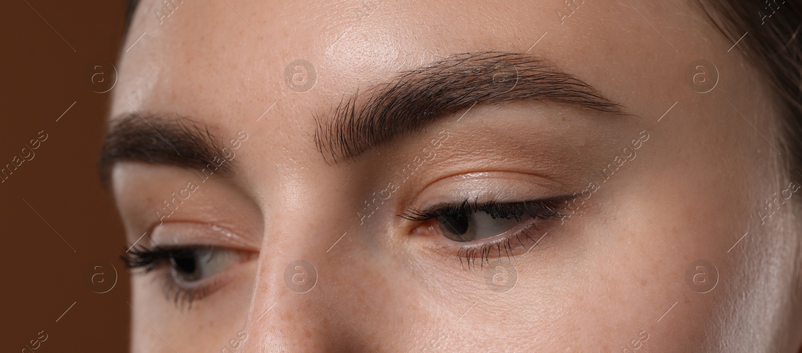 Photo of Young woman with beautiful eyebrows on brown background, closeup