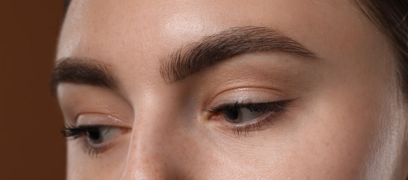 Photo of Young woman with beautiful eyebrows on brown background, closeup