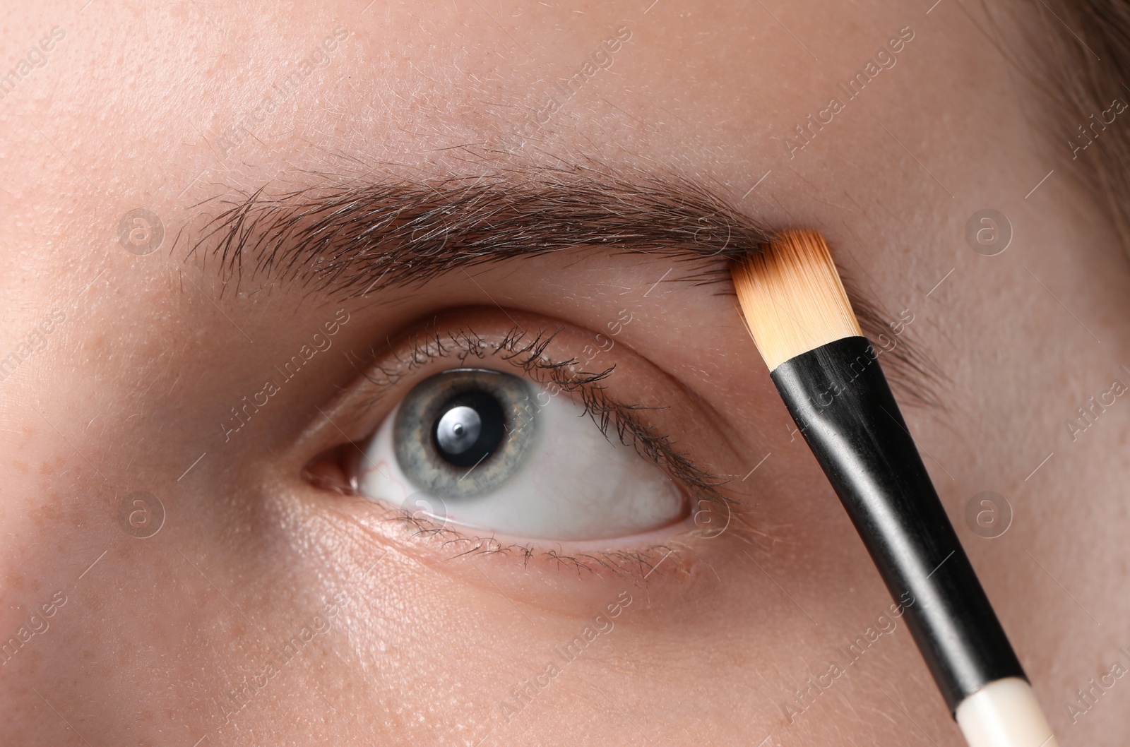 Photo of Young woman applying cosmetic product onto her eyebrow with brush, closeup