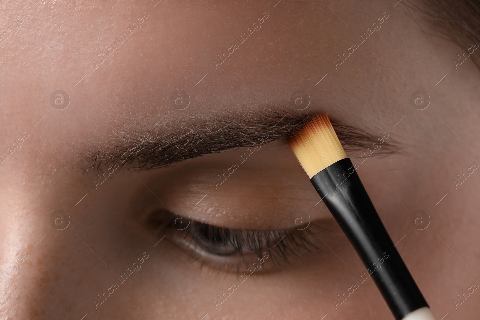 Photo of Young woman applying cosmetic product onto her eyebrow with brush, closeup