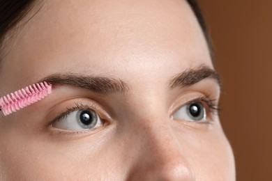 Photo of Young woman brushing her eyebrow with spoolie on brown background, closeup