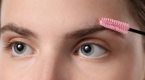 Photo of Young woman brushing her eyebrow with spoolie, closeup