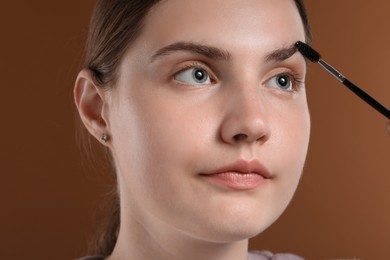 Photo of Young woman brushing her eyebrow with spoolie on brown background, closeup