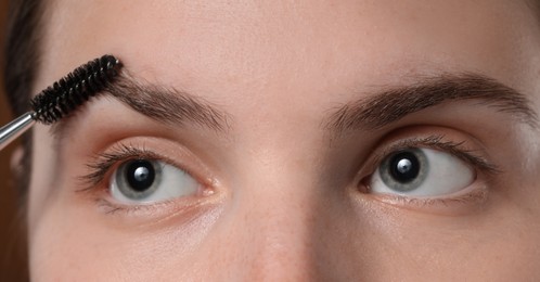 Photo of Young woman brushing her eyebrow with spoolie, closeup