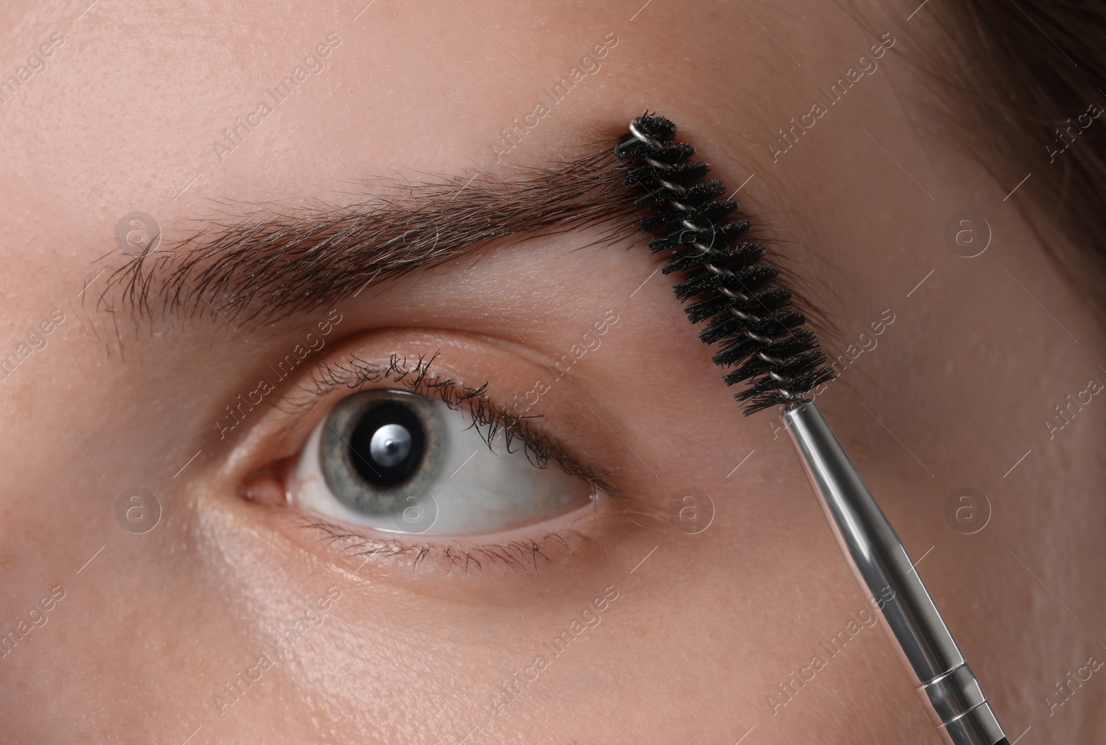 Photo of Young woman brushing her eyebrow with spoolie, closeup