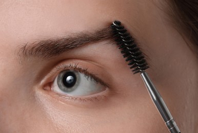 Photo of Young woman brushing her eyebrow with spoolie, closeup