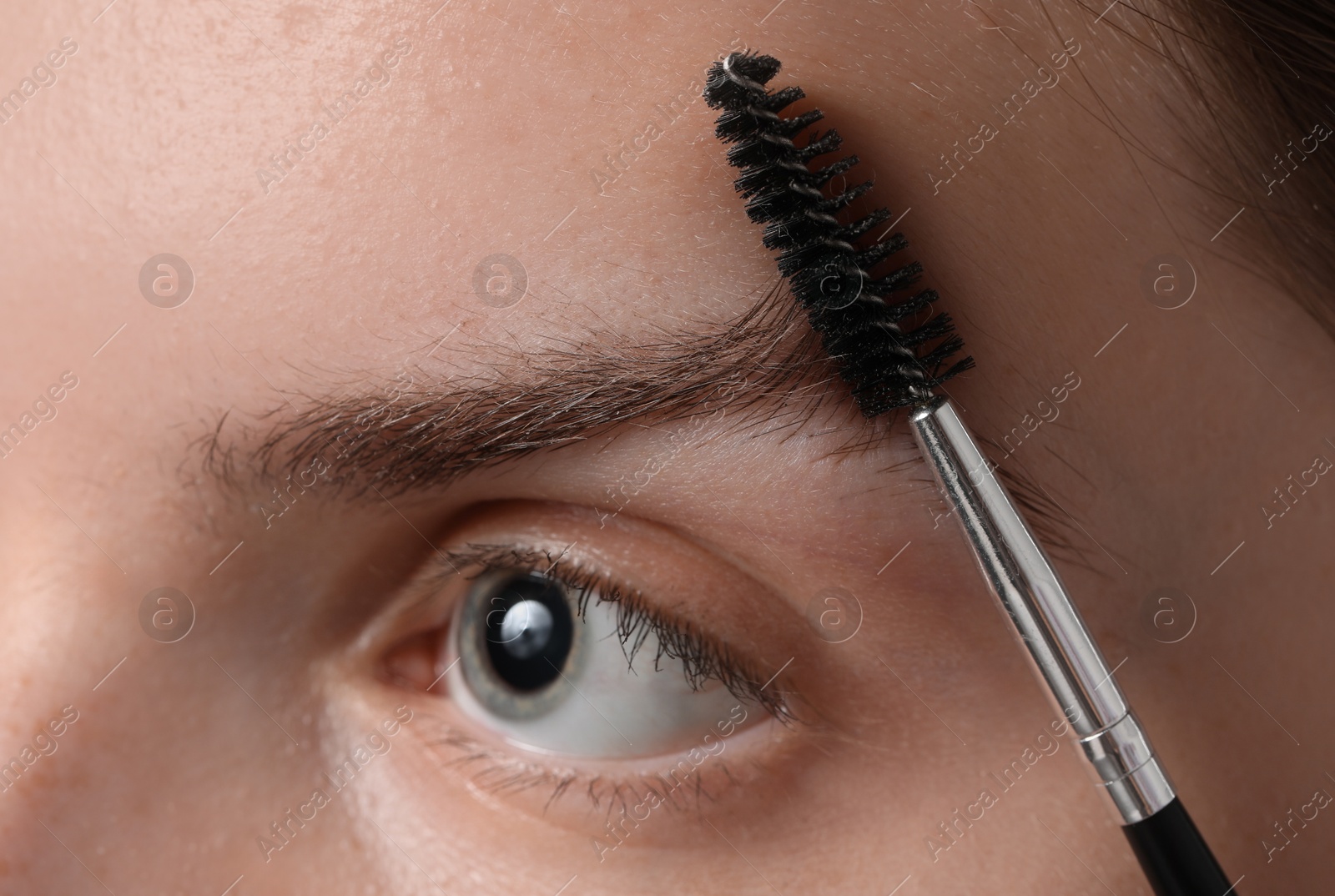 Photo of Young woman brushing her eyebrow with spoolie, closeup
