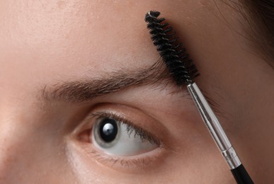 Photo of Young woman brushing her eyebrow with spoolie, closeup