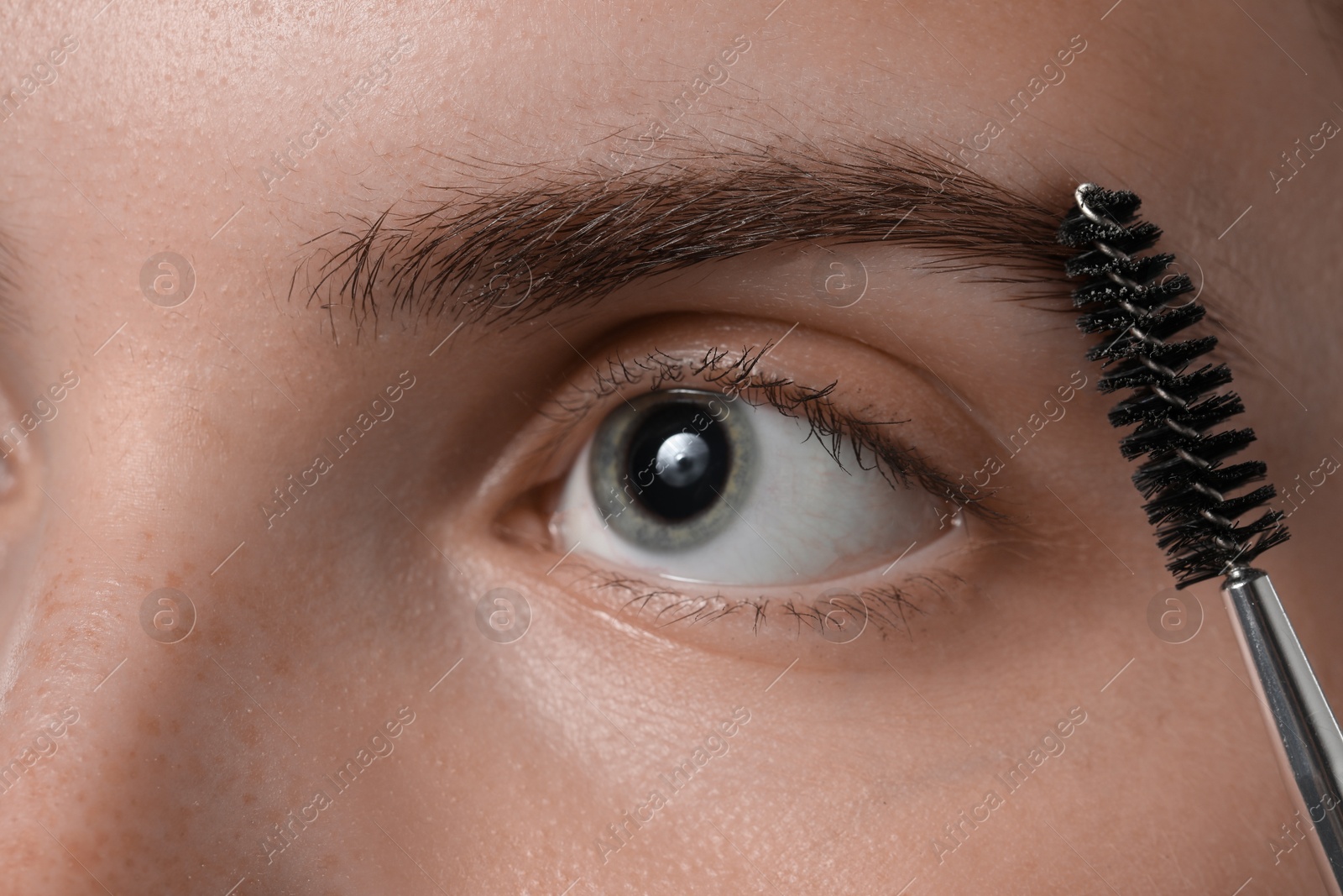 Photo of Young woman brushing her eyebrow with spoolie, closeup