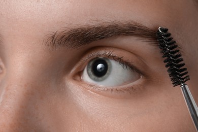 Photo of Young woman brushing her eyebrow with spoolie, closeup