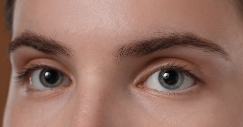 Photo of Young woman with beautiful eyebrows on brown background, closeup