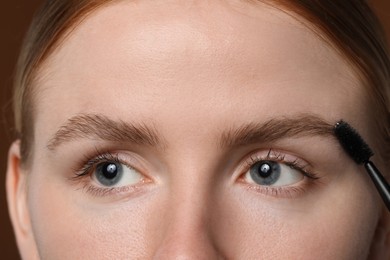 Photo of Young woman brushing her eyebrow with spoolie on brown background, closeup