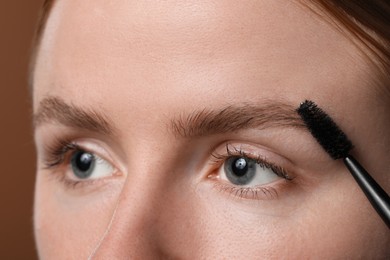 Photo of Young woman brushing her eyebrow with spoolie on brown background, closeup