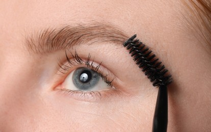 Photo of Young woman brushing her eyebrow with spoolie, closeup
