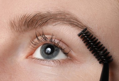 Photo of Young woman brushing her eyebrow with spoolie, closeup