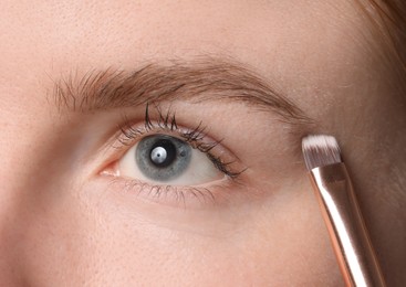 Photo of Young woman applying cosmetic product onto her eyebrow with brush, closeup