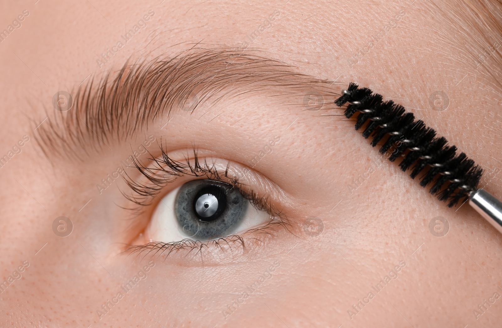 Photo of Young woman brushing her eyebrow with spoolie, closeup