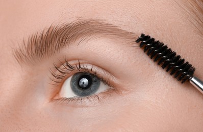 Photo of Young woman brushing her eyebrow with spoolie, closeup