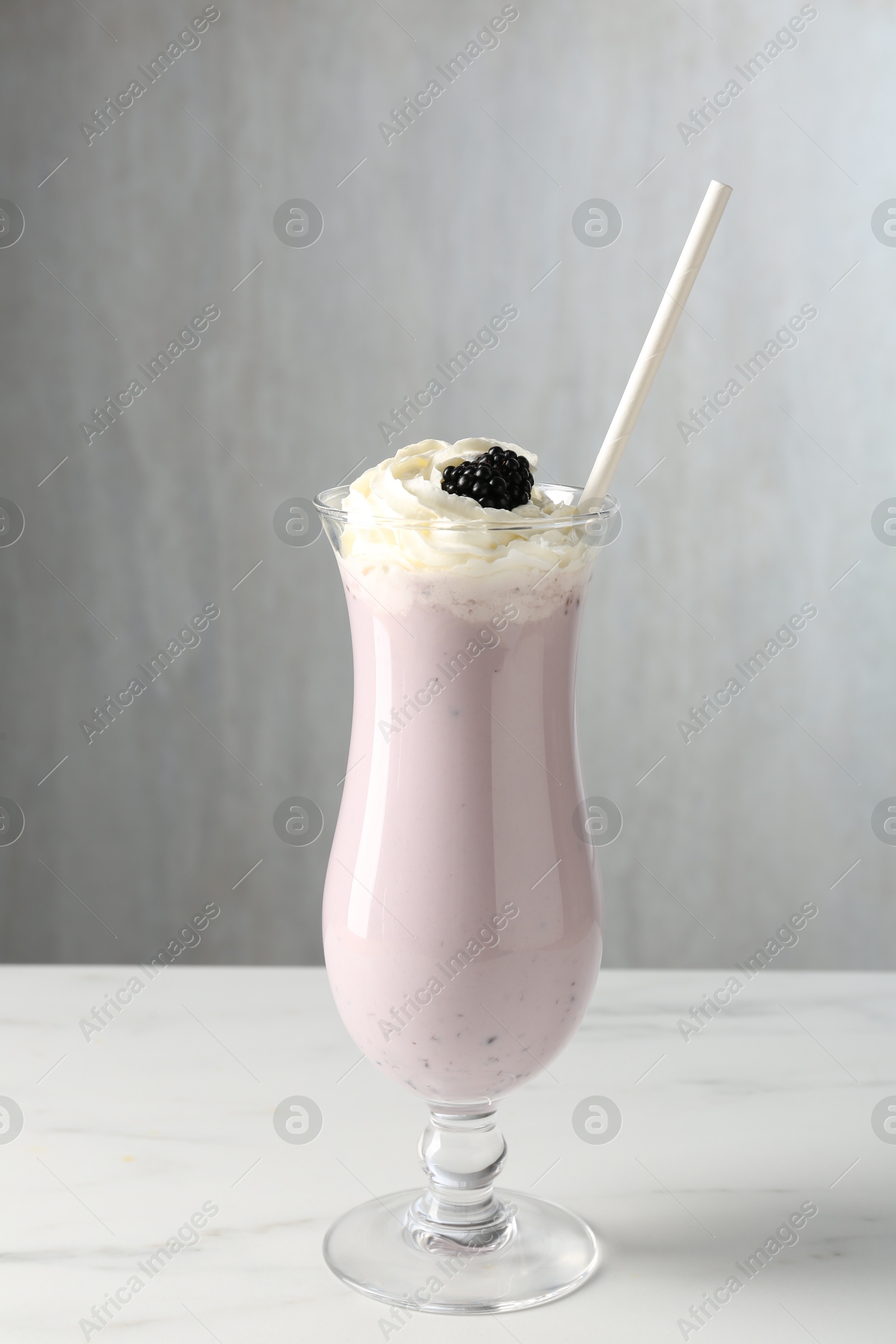 Photo of Tasty blackberry milkshake with whipped cream in glass on white marble table