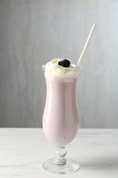 Photo of Tasty blackberry milkshake with whipped cream in glass on white marble table