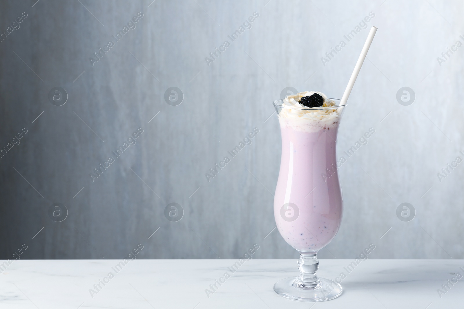 Photo of Tasty blackberry milkshake with whipped cream in glass on white marble table, space for text