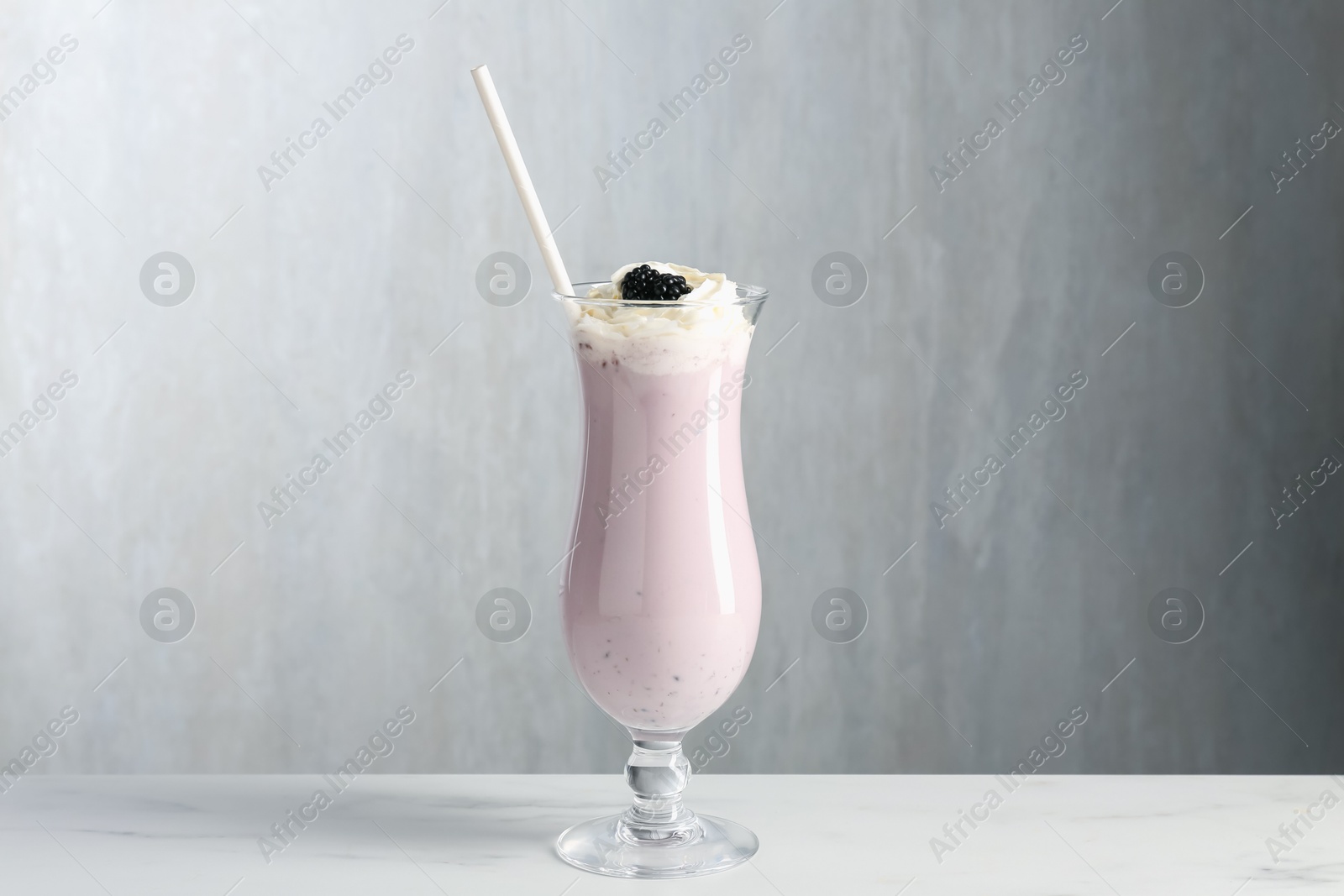 Tasty blackberry milkshake with whipped cream in glass on white marble table Photo of Tasty blackberry milkshake with whipped cream in glass on white marble table