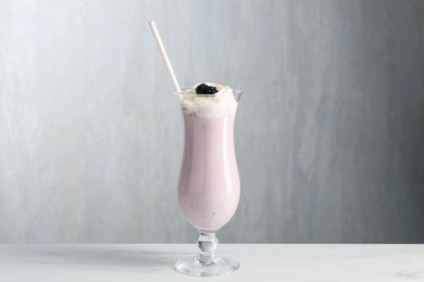 Photo of Tasty blackberry milkshake with whipped cream in glass on white marble table